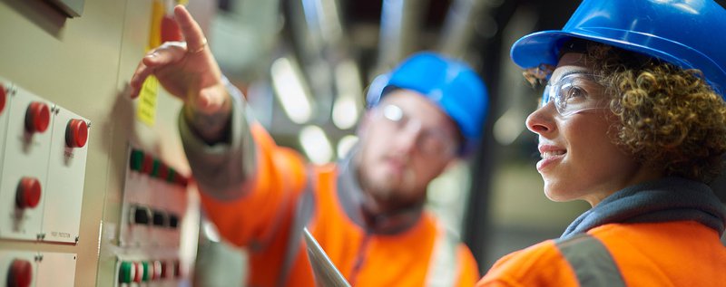 Two people with hard hats working on machinery