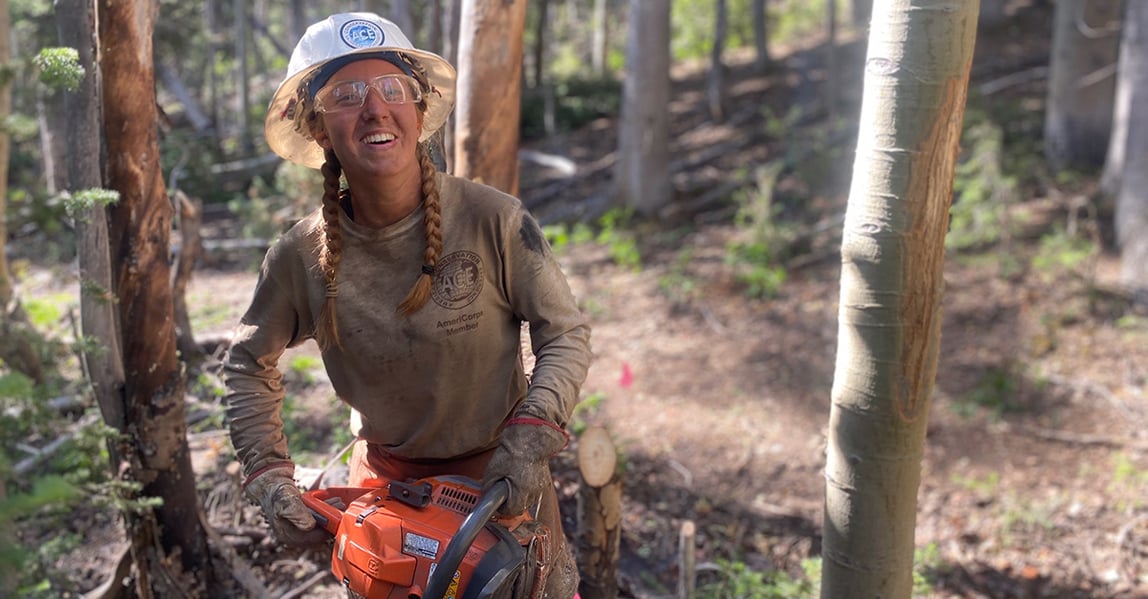Woman in the woods holding a chain saw working and smiling. 