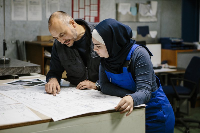 Woman wearing headscarf speaking with a man in a technical work environment