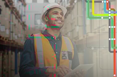 Man wearing a hard hat and safety vest holds a tablet next to shelves of packages
