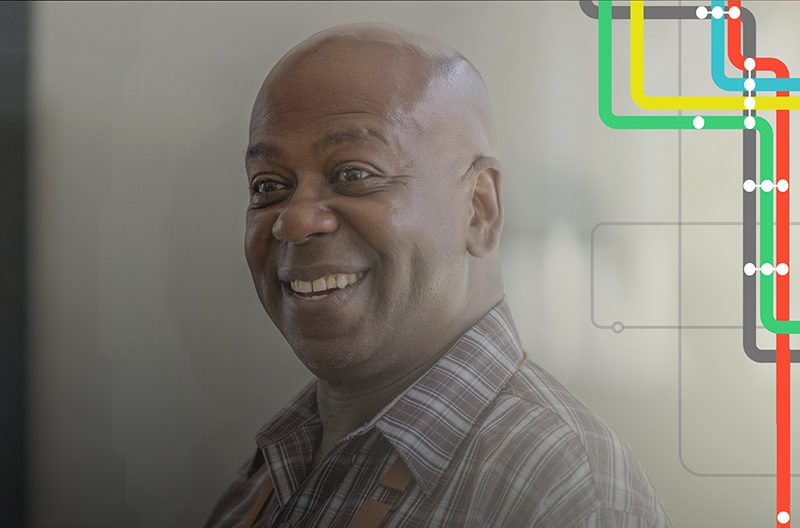 An older black man stands next to the door of his storefront