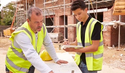 Young construction apprentice taking notes as supervisor explains the blueprint