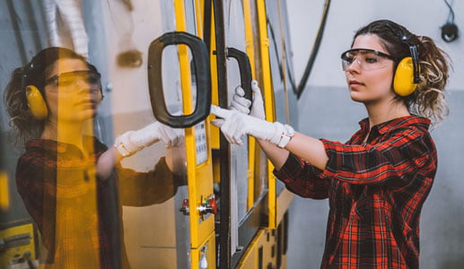 Young woman wearing ear muffs working on machinery