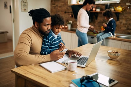 african-american-father-using-smart-phone-while-working-laptop-home