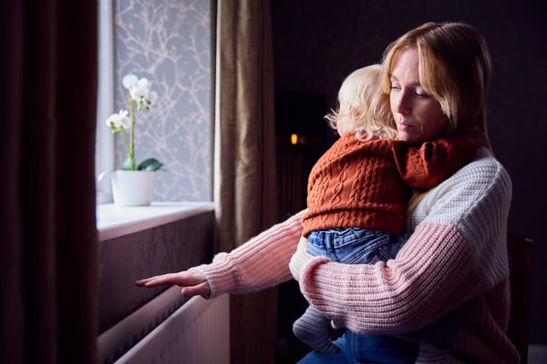 Mother With Son Trying To Keep Warm By Radiator At Home