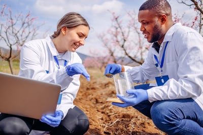 Two young agronomists check the crops in the field using laptop