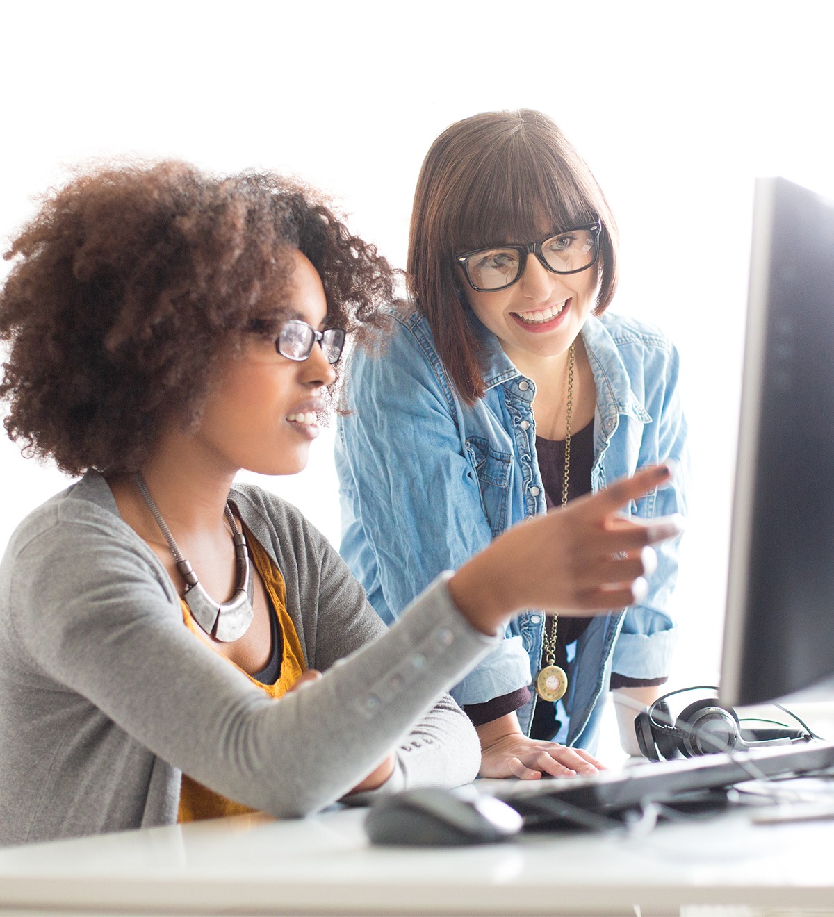 Two women looking at a computer, one person helping the other how to use a specific software